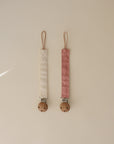 The mushie Linen Pacifier Clip 2-Pack features two linen clips with wooden and silicone clasps, shown side by side on a light beige background in cream and dusty pink colors.