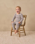 Smiling toddler in Rylee + Cru Ribbed Tee + Legging Set Slate Microstripe on wood chair.