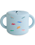 The mushie Snack Cup in Retro Cars features light blue silicone, two handles, and colorful car designs. Made for toddlers, its spill-proof lid with a slit opening allows easy snack access.