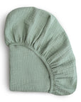 The mushie Extra Soft Bassinet Muslin Crib Sheet in light sage green features elastic edges and gathered corners, offering soft, breathable fabric—ideal for cozy nursery bedding.