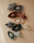 Mushie Bath Boats in muted colors—stackable water play toys on a beige surface.