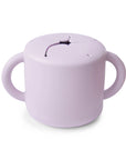 The mushie Snack Cup in Soft Lilac is a spill-proof silicone cup with two handles and a flexible, slotted lid, designed for toddlers to easily access snacks while preventing spills.