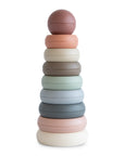 The mushie Stacking Rings Toy features pastel-colored, non-toxic, donut-shaped rings in muted shades, stacked from largest to smallest with a round ball on top.
