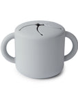 The mushie Snack Cup in Stone is a spill-proof silicone cup for toddlers with two handles and a flexible petal lid, allowing easy access for little hands while keeping snacks secure.