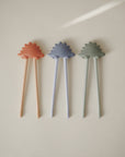Three mushie training chopsticks for toddlers in pastel colors on a light background.