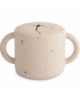 The mushie Snack Cup in Vanilla Confetti features two handles and a flexible slit lid for easy, spill-proof snacking on the go.