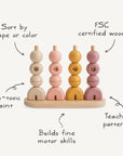 The Mushie Wooden Multi Shape Stacker features four rods with assorted shapes and colors. FSC certified wood, non-toxic paint, and handwritten labels emphasize sorting by shape or color and building fine motor skills.