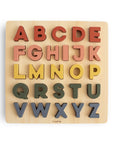 The Mushie Wooden Puzzle features raised, colorful uppercase letters in earthy tones, making it a fun educational toy that helps children learn their ABCs and develop fine motor skills.