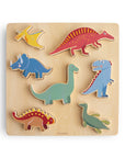 The Mushie Wooden Puzzle includes seven colorful dinosaur pieces—pterodactyl, triceratops, stegosaurus, spinosaurus, brachiosaurus, tyrannosaurus, and plesiosaur—that help kids build fine motor skills as they fit them onto a light wood board.