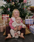 Two kids by a Christmas tree with mushie’s Shape Sorting Box, gifts, and holiday cheer.