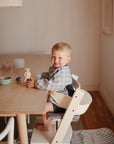 Smiling toddler plays with a mushie HexaPop Suction Toy in a high chair at the table.