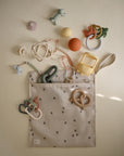 The mushie Water Resistant Wet Bag, beige with black floral prints, is open and spilling out pastel baby toys. Ideal for diaper bag storage, it keeps essentials organized and protected from moisture.