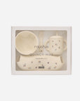 Mushie x Quincy Mae Feeding Kit in a white gift box with a clear window, containing a cream-colored bowl, sippy cup with straw, spoon, and small footmuff.