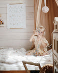 Young girl plays with mushie's HEX Connect Building Toy Set on a bed in a cozy bedroom.