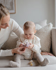 A woman and baby examine a mushie Figurine Teether together while sitting on a sofa.