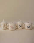 Four cream-colored ceramic mugs with handles and straws, each featuring delicate floral or bird designs, are arranged in a row on a beige background—perfectly complementing the mushie Snack Cup for your toddler.