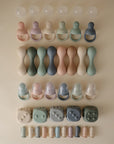 Mushie Silicone Baby Rattle Toy, crafted from food-grade silicone and arranged in rows, offers a gentle sensory experience in soft pastel shades of beige, pink, blue, green, and gray.