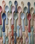 The mushie Silicone Toddler Starter Spoons are neatly displayed in pastel blue, pink, green, and beige on a light background—perfect for encouraging independent feeding.