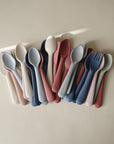 The mushie Dinnerware Fork and Spoon Set features neatly arranged pastel pink, blue, and beige utensils made from non-toxic plastic, displayed on a neutral surface.