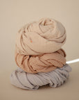 Three mushie Extra Soft Muslin Crib Sheets in neutral tones for breathable baby bedding.