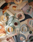 Mushie Dinnerware Cups, along with pastel silicone bibs and plates featuring star and moon patterns, create a charming, non-toxic mealtime set for babies.