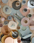 A top view of mushie Dinnerware Cups arranged with pastel baby plates, bibs, and utensils on a table, forming a soft and playful pattern.