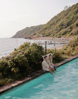 Two kids in mushie Bear Robe sit by a pool with sea and hills in the background.