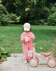Toddler with Mushie Silicone Training Cup + Straw stands by a pink tricycle in the park.