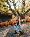A young girl in a skeleton costume walks along an autumn-leaf-covered path, carrying a mushie Water Resistant Wet Bag, with pumpkins behind her and sunlight streaming through the trees.