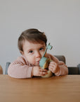 Toddler enjoys mess-free feeding at the table with the mushie Silicone Puree Pouch.