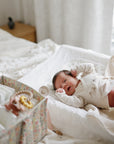 Newborn on bed next to mushie Extra Soft Muslin Changing Pad Cover and baby supply box.