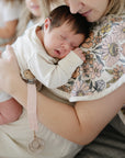 Newborn in arms, mushie Linen Pacifier Clip 2-Pack with silicone clasp visible nearby.