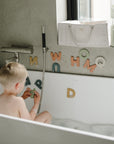 Young child playing with mushie Letters & Numbers Bath Play Set in the bathtub.