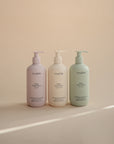 Three mushie Baby Body Lotions in pastel bottles with natural ingredients on a neutral background.