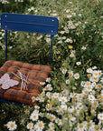 Blue chair with daisies, brown cushion, colored pencils, and mushie Silicone Sensory Toy on seat.