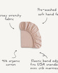 The mushie Stretchy MINI Crib Sheet in light pink is made from 95% organic cotton jersey, pre-washed for softness, breathable comfort, and features an elastic band edge. Product features are shown on a clean background.