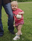 Toddler with FRIGG Daisy Natural Rubber Pacifier beside adult on green grass outdoors.