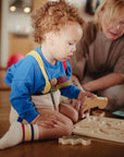 A toddler assembles a Mushie Wooden Puzzle as an adult assists with the FSC-certified toy.