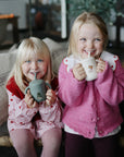 Two smiling girls enjoy sipping from Mushie Silicone Training Cups + Straws.
