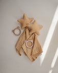 Two mushie Star Lovey Blankets in soft yellow rest on a light surface with matching organic cotton cloths. Nearby are two animal ear-shaped baby teethers, one beige and one pink, all displayed in gentle natural lighting.