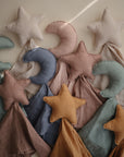 The mushie Moon Lovey Blanket, made with soft organic cotton and featuring pastel star and crescent toys, is displayed on a neutral background.