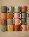 Four columns of four small, colorful mushie Snack Cups are stacked in a grid. With pastel tones and both solid, speckled, or marbled designs, they evoke the cheerful look of toddler snack cups.