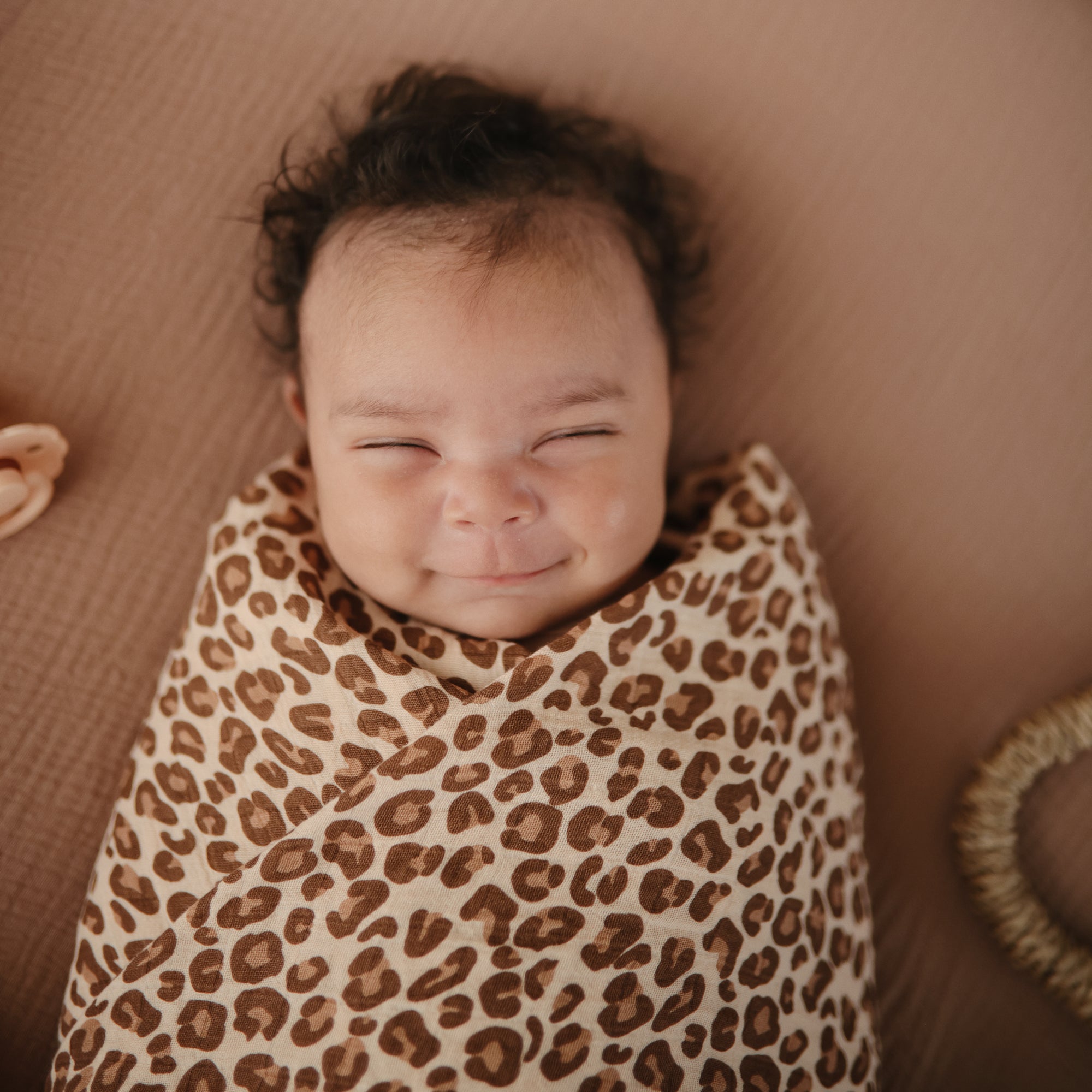 Lifestyle image of a baby swaddled in organic cotton swaddle in Leopard