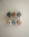 Six mushie Snack Cups with handles are arranged in two rows on a light surface. Each pastel-colored, spill-proof cup has a flower-shaped slit lid in muted green, beige, blue, pink, and tan.