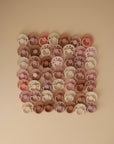 A grid of FRIGG Andersen Fairytale Silicone Pacifier 2-Pack, pastel-colored in pink, beige, and brown, made in Denmark, arranged neatly on a beige background.