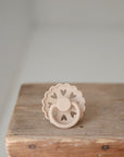 The FRIGG Andersen Fairytale Silicone Pacifier 2-Pack by FRIGG features a beige pacifier with a scalloped edge and heart-shaped cutouts, shown upright on rustic wood against a light background. Expertly crafted in Denmark.