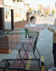 A woman smiles as she pushes a shopping cart outside on a sunny day, her baby cozy in the seat under a leopard-print mushie Multi-Use Cover.