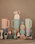 The mushie Silicone Baby Rattle Toy is displayed against a beige background, highlighting its modern, minimalist design and soft pastel colors.