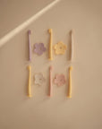 Six pastel mushie Flower Training Toothbrushes with three flower-shaped holders are arranged neatly on a beige background under soft, natural light. Ideal as baby toothbrushes or for training toddlers.