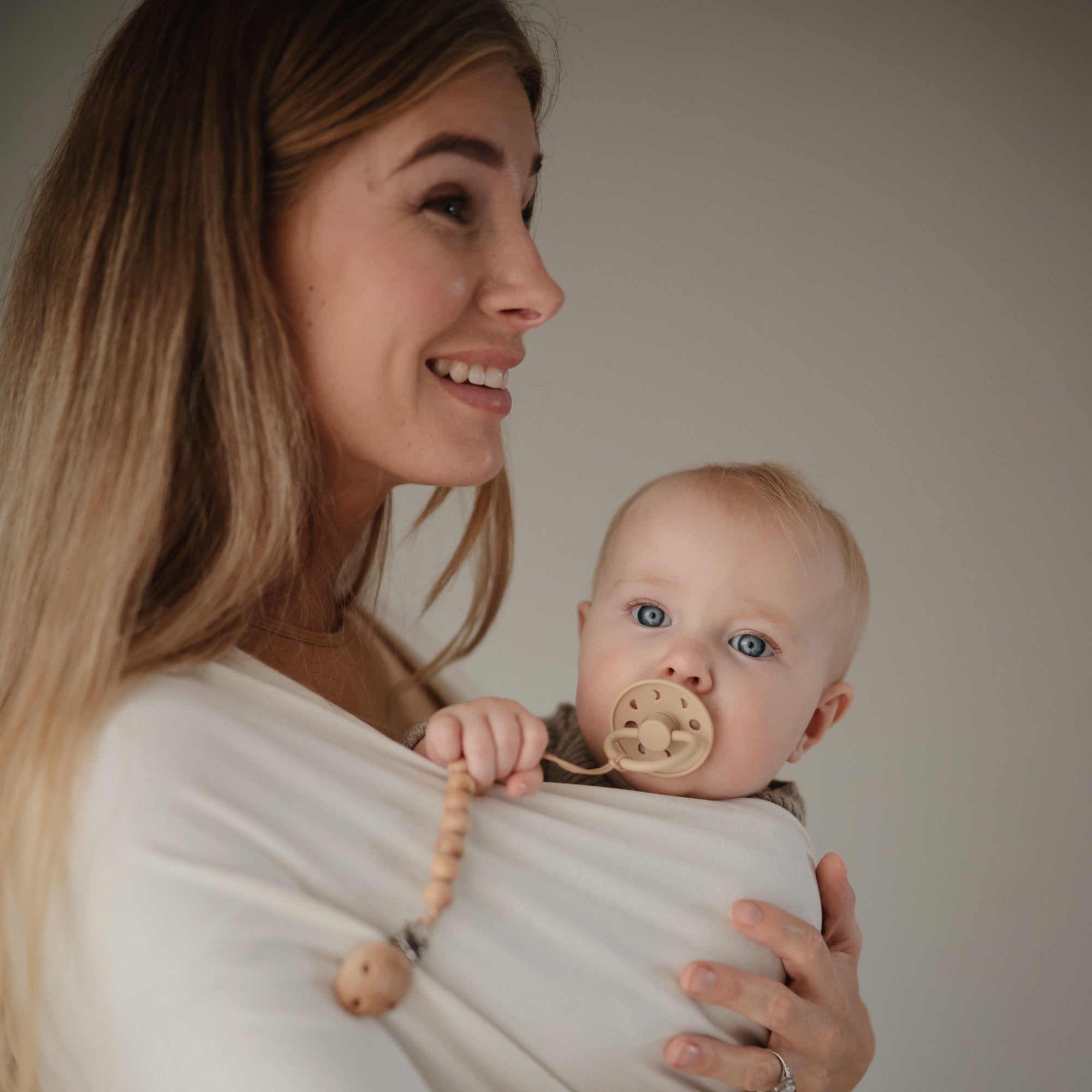 Lifestyle image of a mother and baby in the Mushie Baby Wrap with a Moon pacifier.